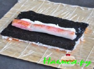Лист перевернуть икрой вниз на пищевую пленку. Сверху на нори выложить измельченные крабовые палочки и творожный крем