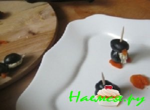 В целые маслины осторожно вставить треугольнички из морковки, проткнуть их деревянной шпажкой, после чего соединить голову с фаршированными маслинами (туловищем) и основой из морковки (лапками)